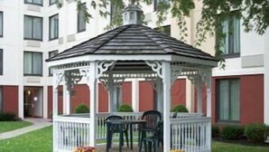 A gazebo with a white railing and a tiled roof, surrounded by grass and potted plants. - Ramada by Wyndham Watertown/Thousand Islands NY (Watertown)