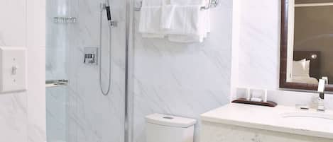 A modern bathroom with a glass-enclosed shower, a toilet, and a marble sink with a mirror.