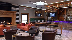 A hotel lobby with leather sofas, a fireplace, a bar area, and a television screen.