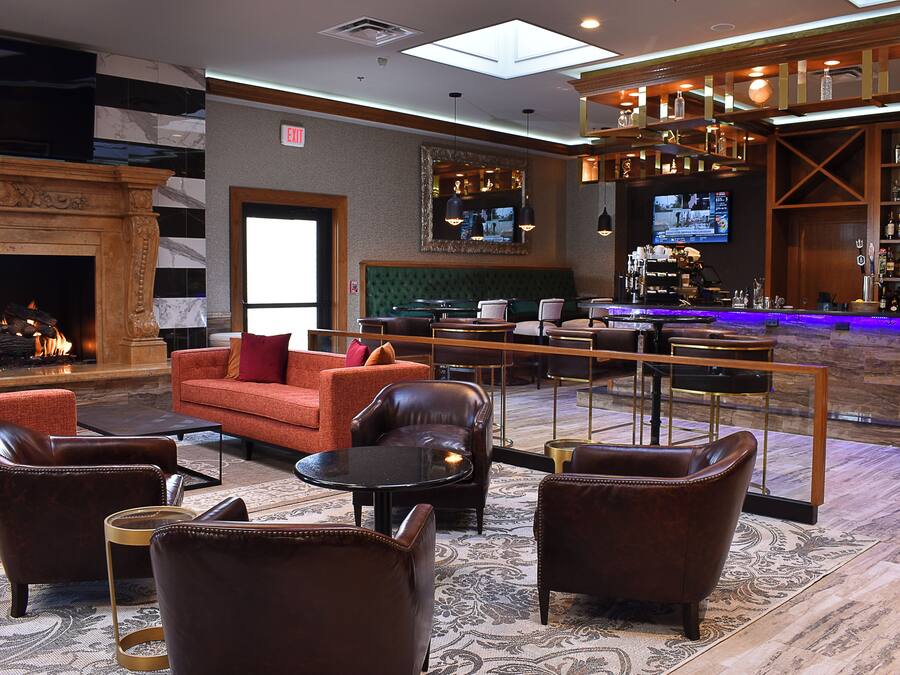 A hotel lobby with leather sofas, a fireplace, a bar area, and a television screen.