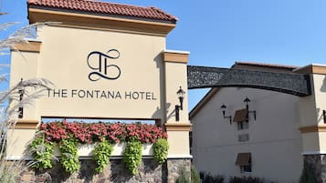 The exterior of The Fontana Hotel with a stone facade, a sign with the hotel's name, and a decorative archway.