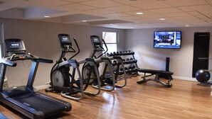 A gym with treadmills, elliptical machines, and a TV screen displaying workout content.