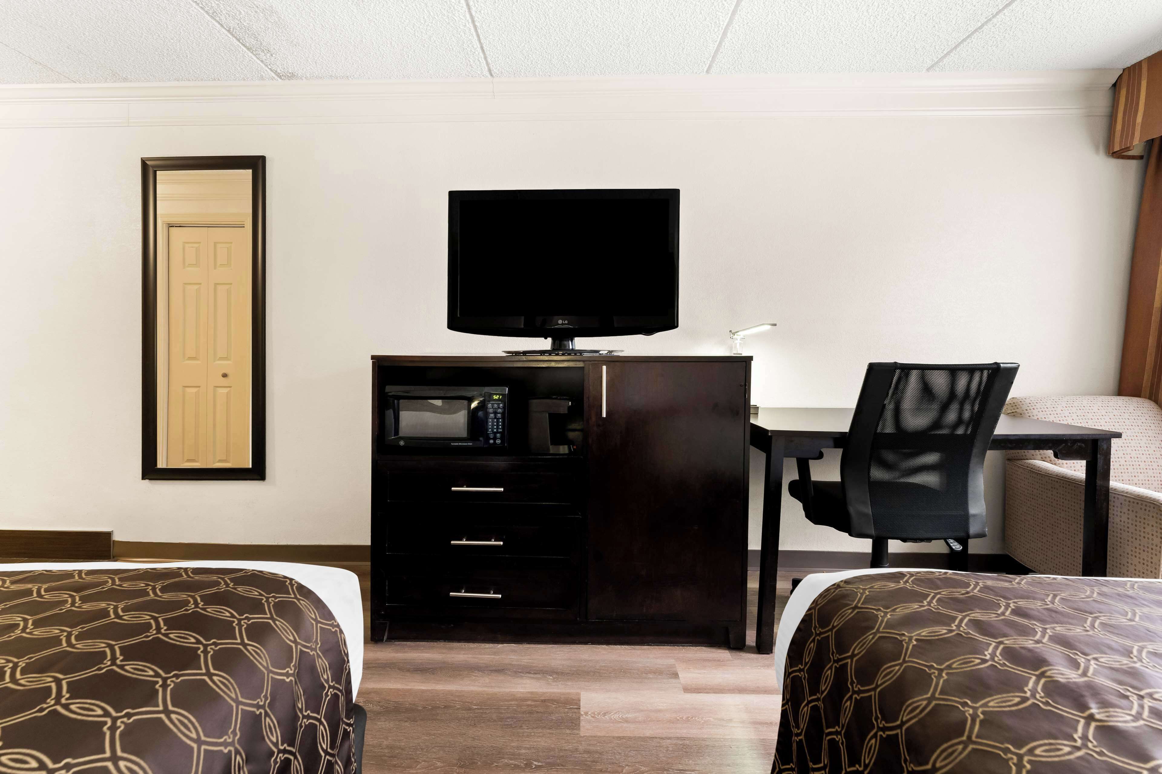 A hotel room with two beds, a desk with a TV, a chair, and a minibar.