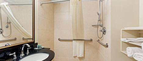 Un baño con lavamanos, espejo, ducha y toallero.