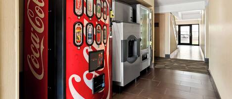 A hallway with a Coca-Cola vending machine and a refrigerator.