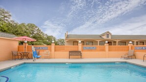 Une piscine entourée d’une clôture en bois agrémentée de panneaux indicateurs, avec des chaises longues et un banc à proximité.