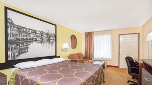 Une chambre d’hôtel avec un grand lit, un bureau, une chaise, une lampe de bureau, une fenêtre avec des rideaux et un tableau encadré au mur.