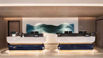A modern hotel reception area with two reception desks, a large abstract wall art piece, and a wooden ceiling.