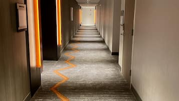 A long, narrow hotel corridor with a patterned carpet and wall-mounted light fixtures.