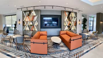 A modern lobby with a large TV, comfortable seating, and decorative shelving.