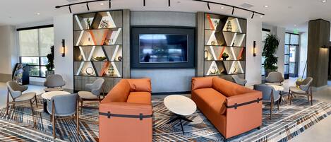 A modern lobby with a large TV, comfortable seating, and decorative shelving.