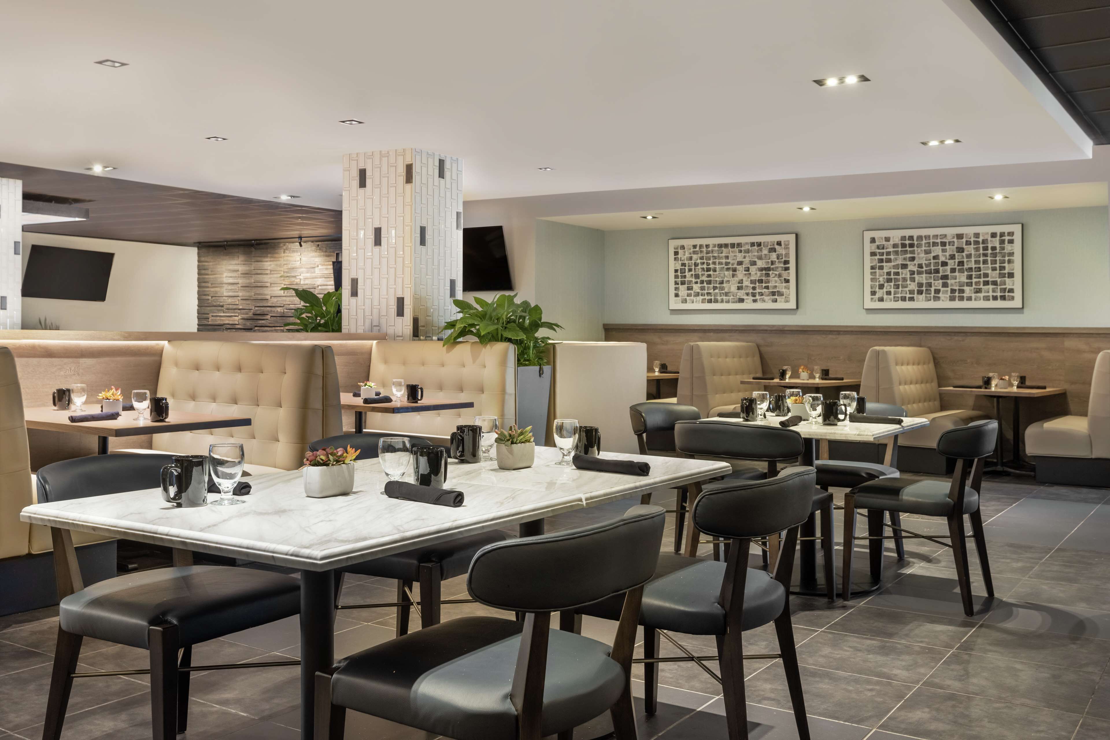 A modern restaurant with marble-topped tables, black chairs, and cushioned booths.
