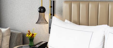 A neatly arranged hotel room with a bed, a bedside table with a lamp, a vase of flowers, and a telephone.