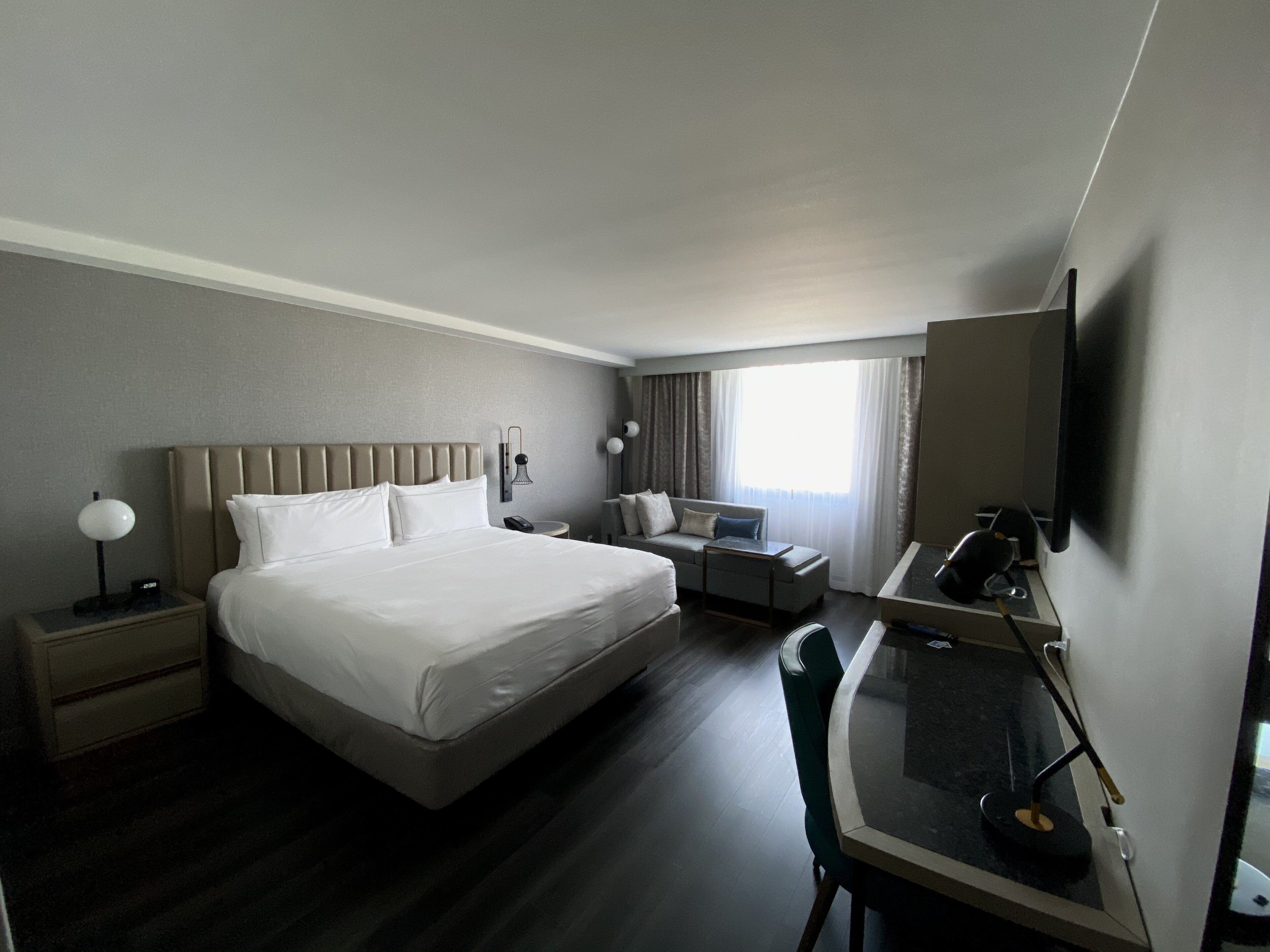 A hotel room with a large bed, a desk with a chair, a TV, and a window with curtains.