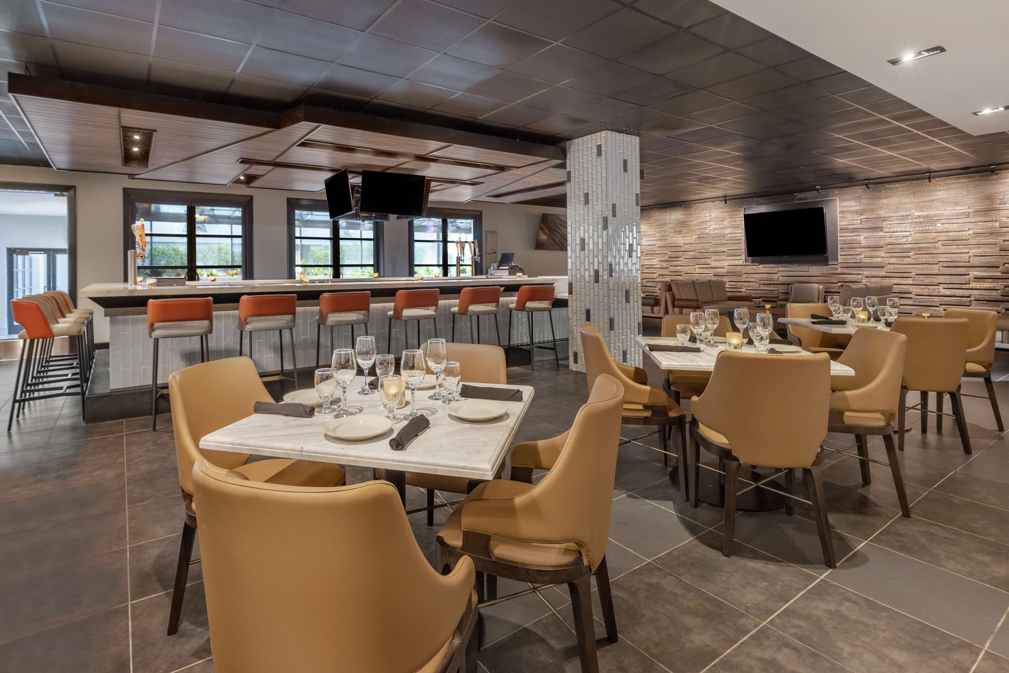 A modern dining area with bar seating, tables set for dining, and a large TV mounted on the wall.