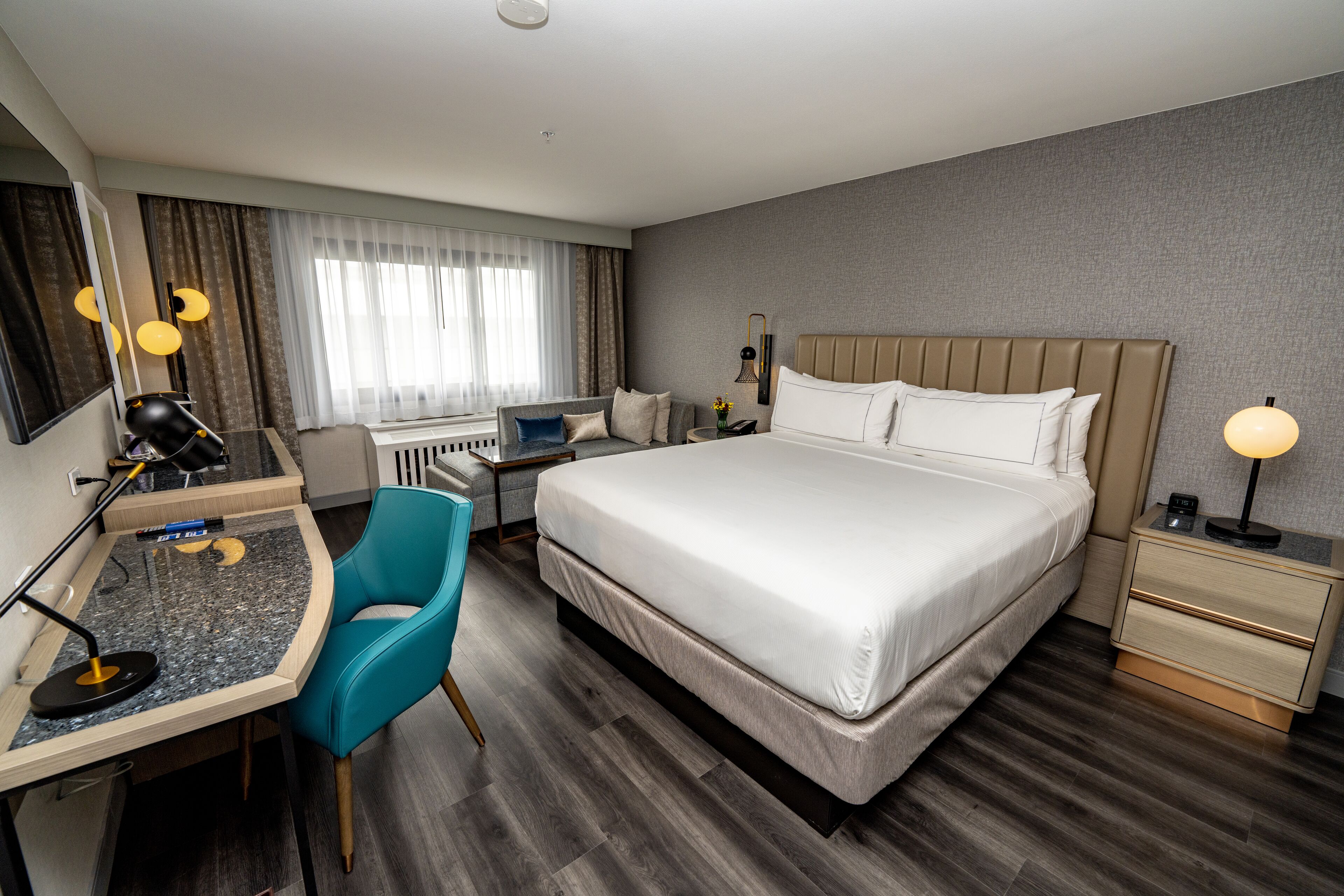 A hotel room with a large bed, a desk with a chair, a small table with a lamp, and a nightstand with a lamp.
