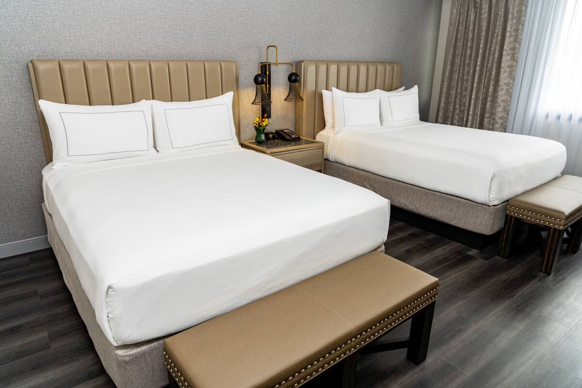 A hotel room with two beds, a bench, and a nightstand with a lamp.