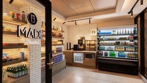 Interior de cafeteria com placa da marca, prateleiras cheias de lanches, máquina de café e balcão refrigerado.