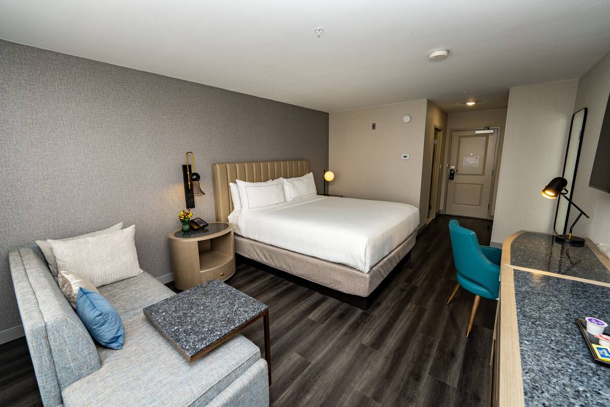A hotel room with a bed, a sofa, a small table, a desk, and a chair.