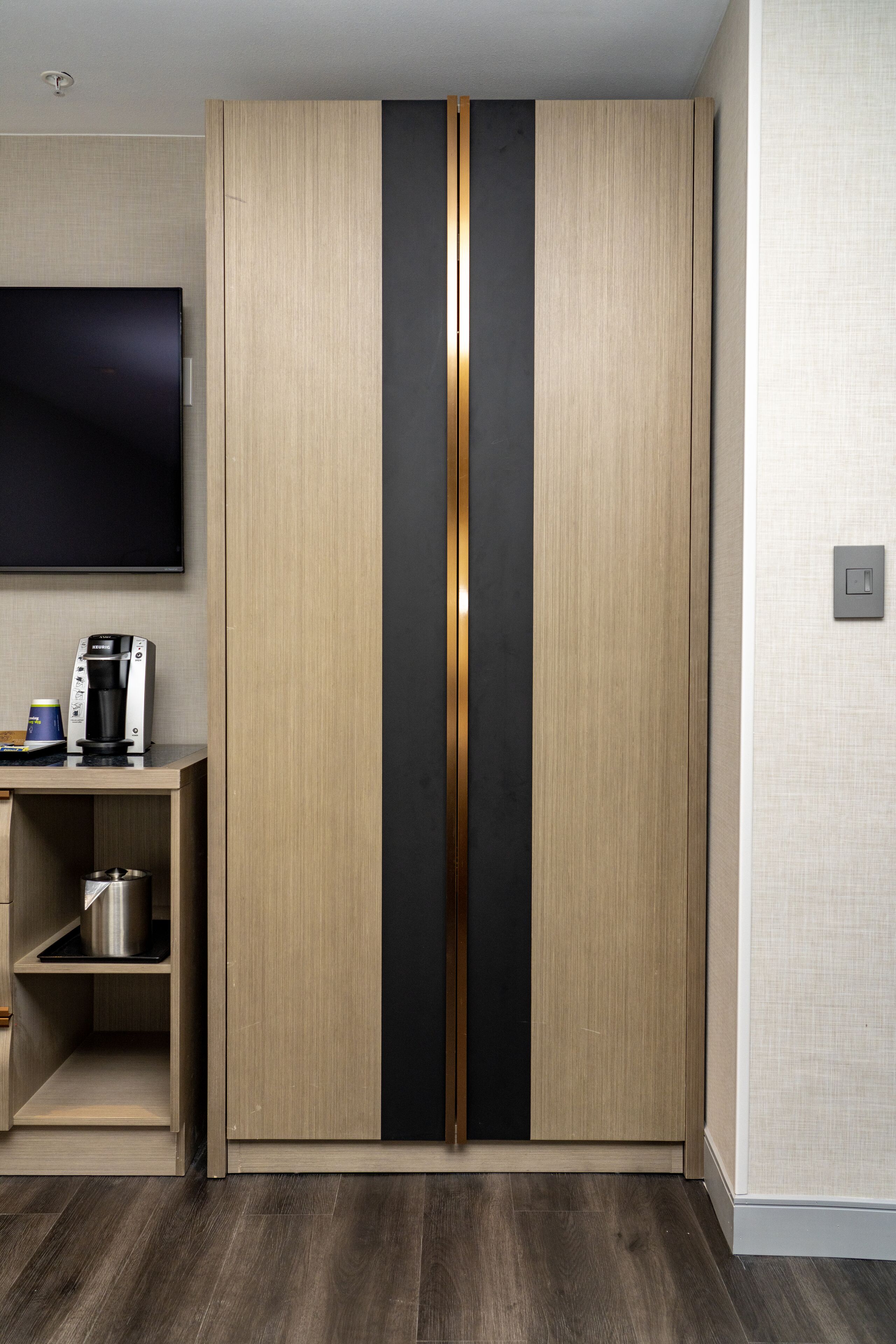 A modern room with a wardrobe, a flat-screen TV, a coffee machine, and a shelf with a pot.