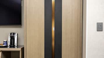 A modern room with a wardrobe, a flat-screen TV, a coffee machine, and a shelf with a pot.