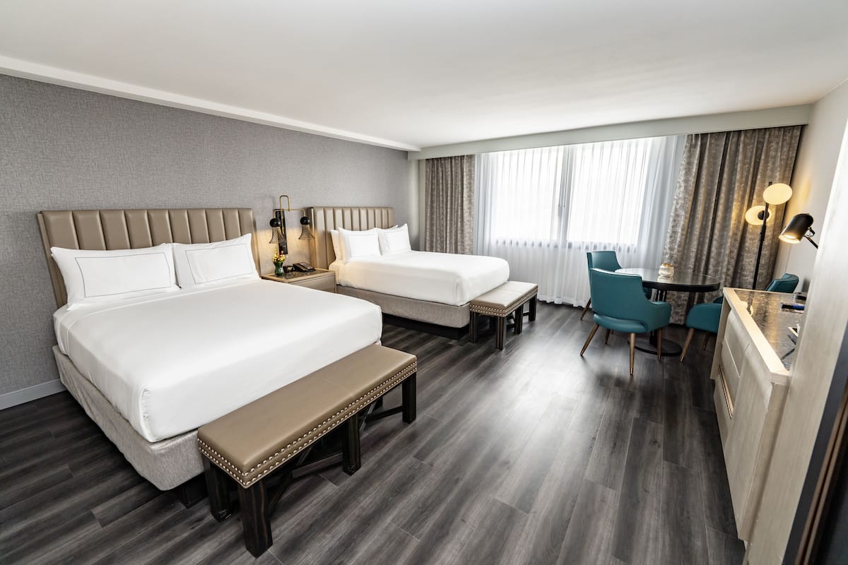 A hotel room with two beds, a bench, a desk, and a chair.