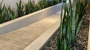 Um interior moderno com um longo banco, arte decorativa na parede e um vaso com plantas verdes grandes.