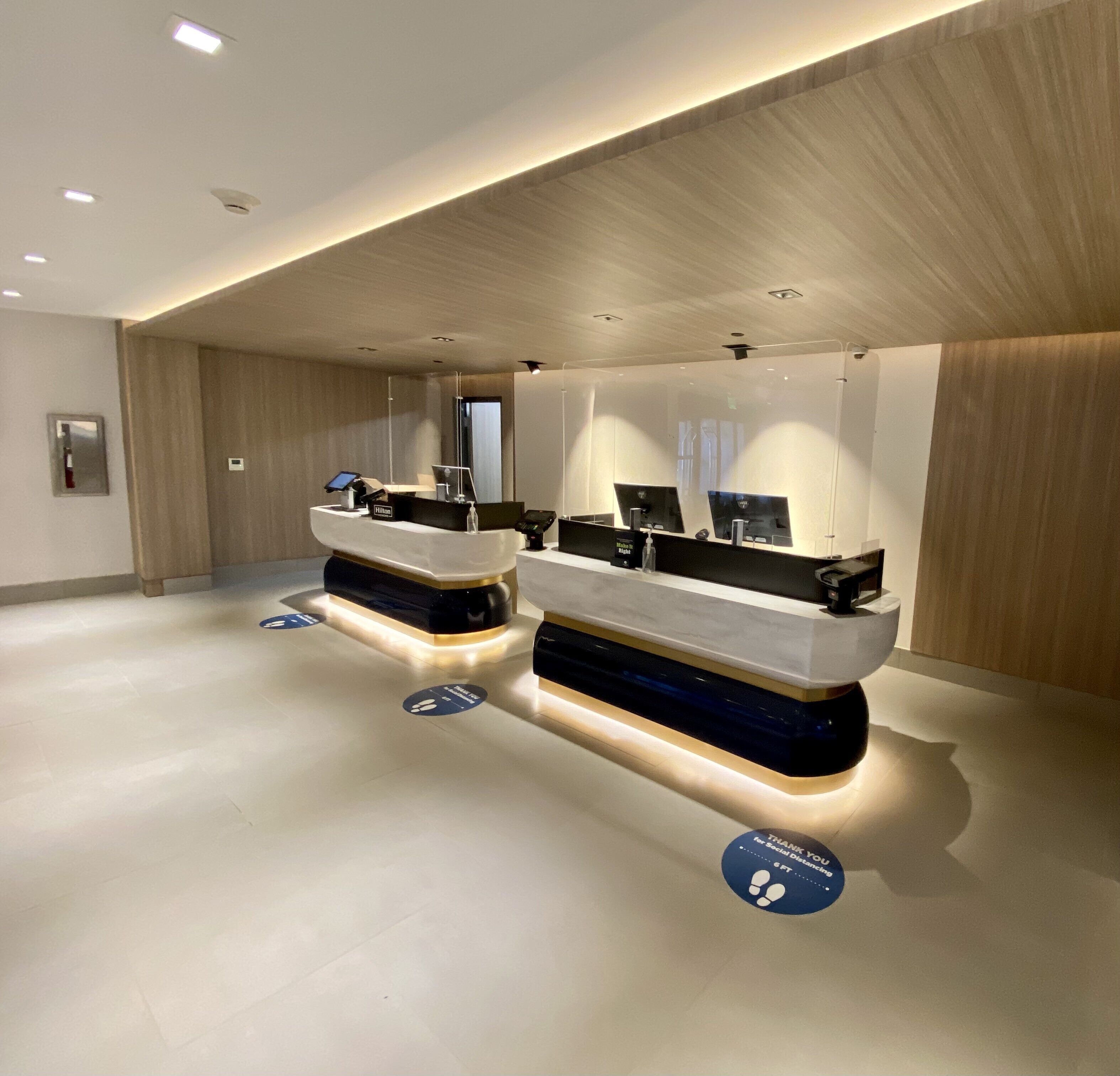 Ein moderner Hotel-Empfangsbereich mit zwei Theken, digitalen Bildschirmen und einem minimalistischen Design.