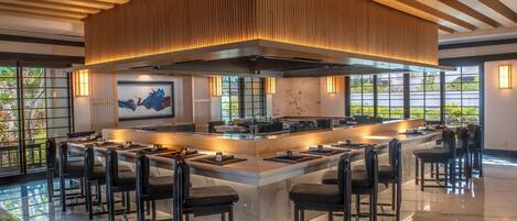 Una cocina moderna con una isla central, taburetes de bar y un amplio ventanal con vistas a zonas verdes.