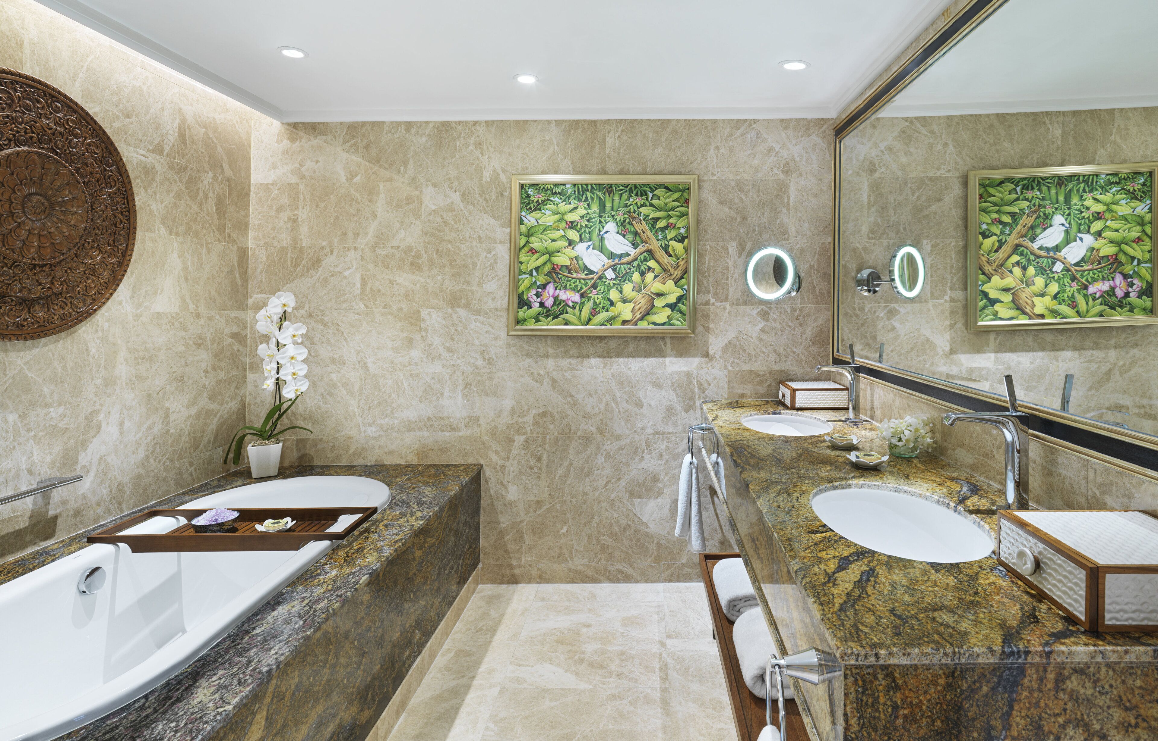 A modern bathroom with a large bathtub, two sinks, marble walls, and decorative paintings.