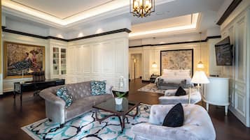 A spacious living room with a large sofa, a coffee table, and a patterned rug. There are two armchairs, a side table, and a painting on the wall.