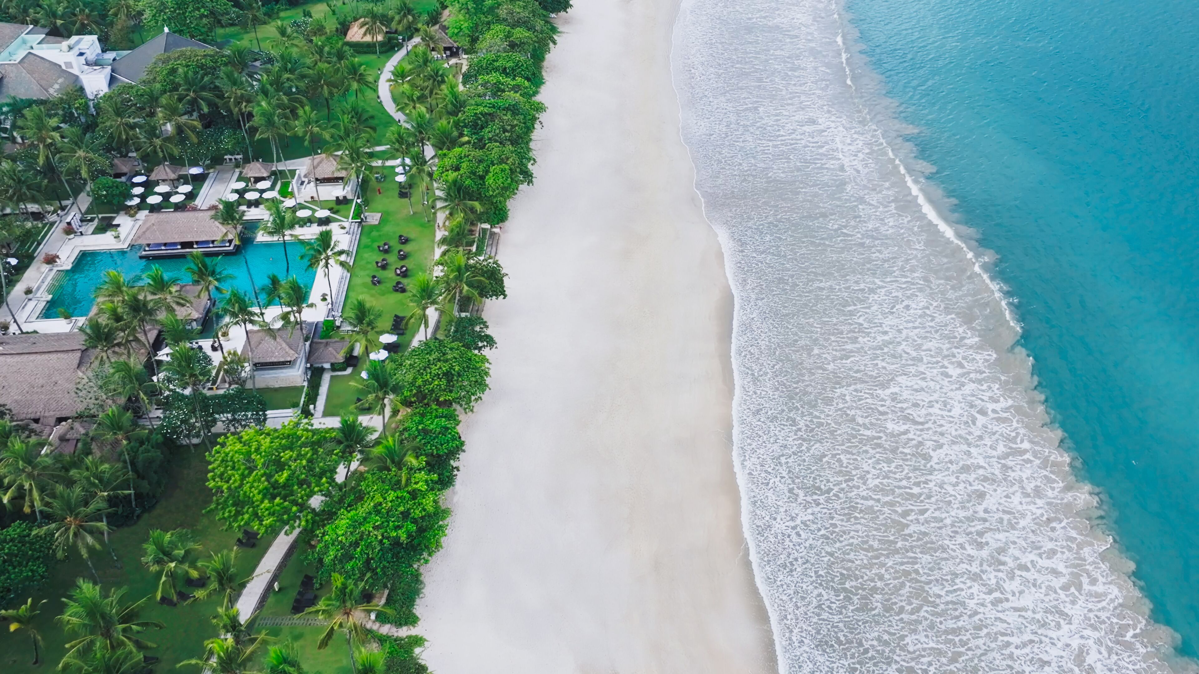 Vista aérea de un resort con una piscina grande, acceso a la playa y abundante vegetación.