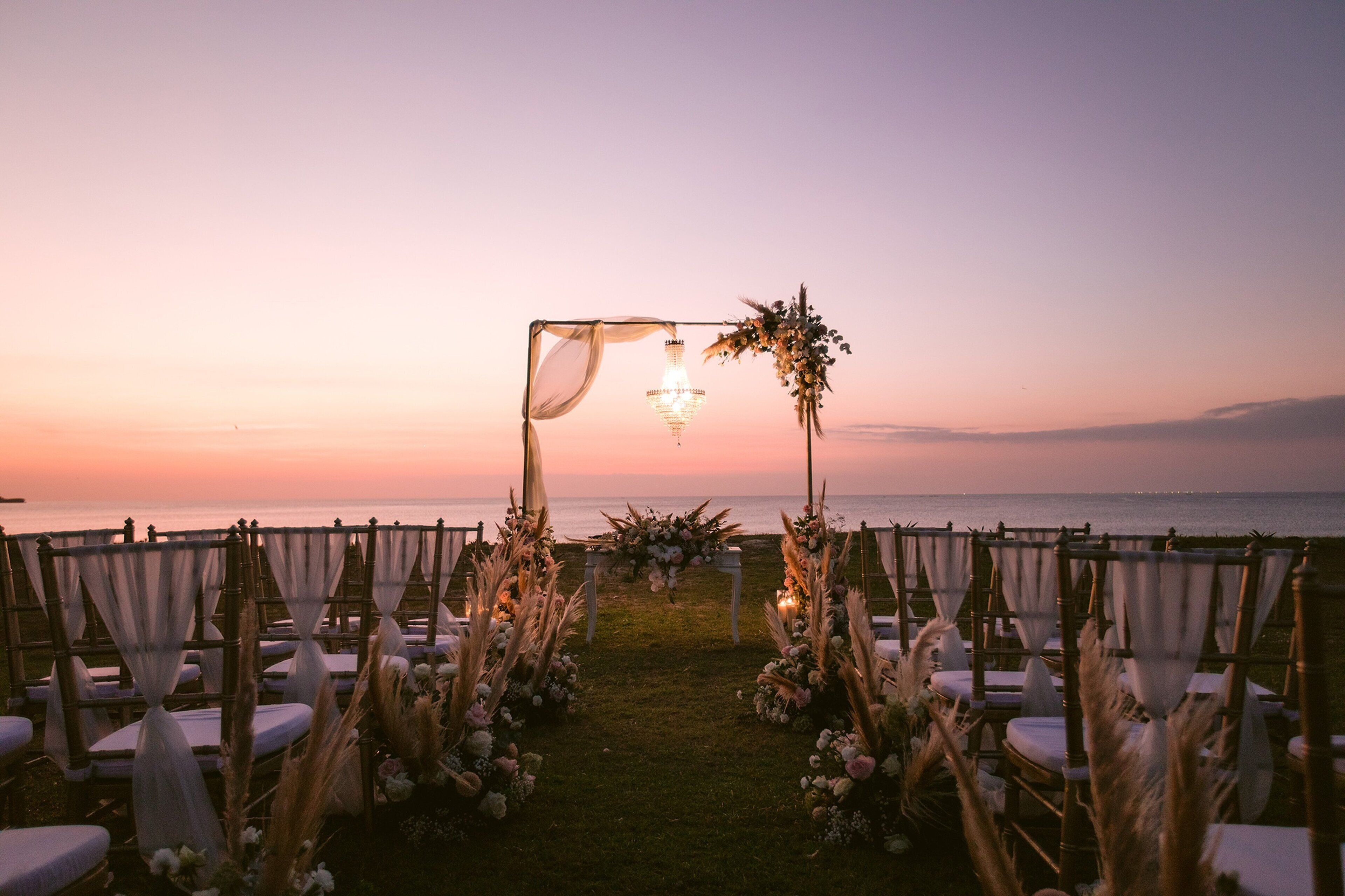 A wedding aisle with chairs and a floral arch at sunset.