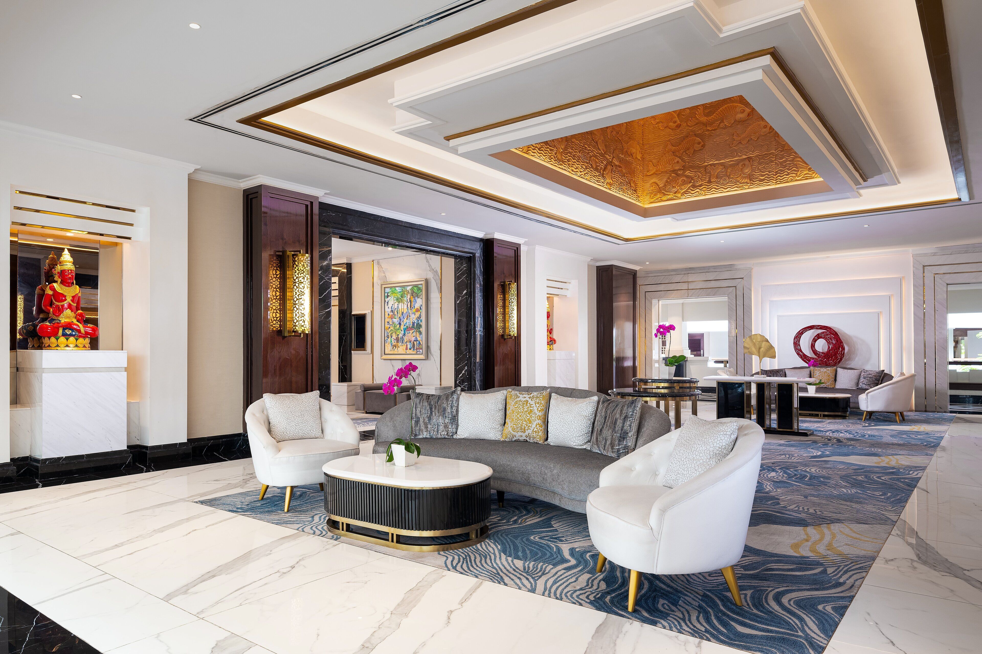 A spacious lobby with a marble floor, a large sofa, white armchairs, and a round coffee table.
