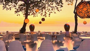 An outdoor dining area with wicker furniture and large vases, overlooking a body of water during sunset. - InterContinental Bali Resort by IHG (Jimbaran)