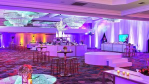 Un espace événementiel spacieux et élégamment décoré, comprenant un bar, des tables rondes et une scène.