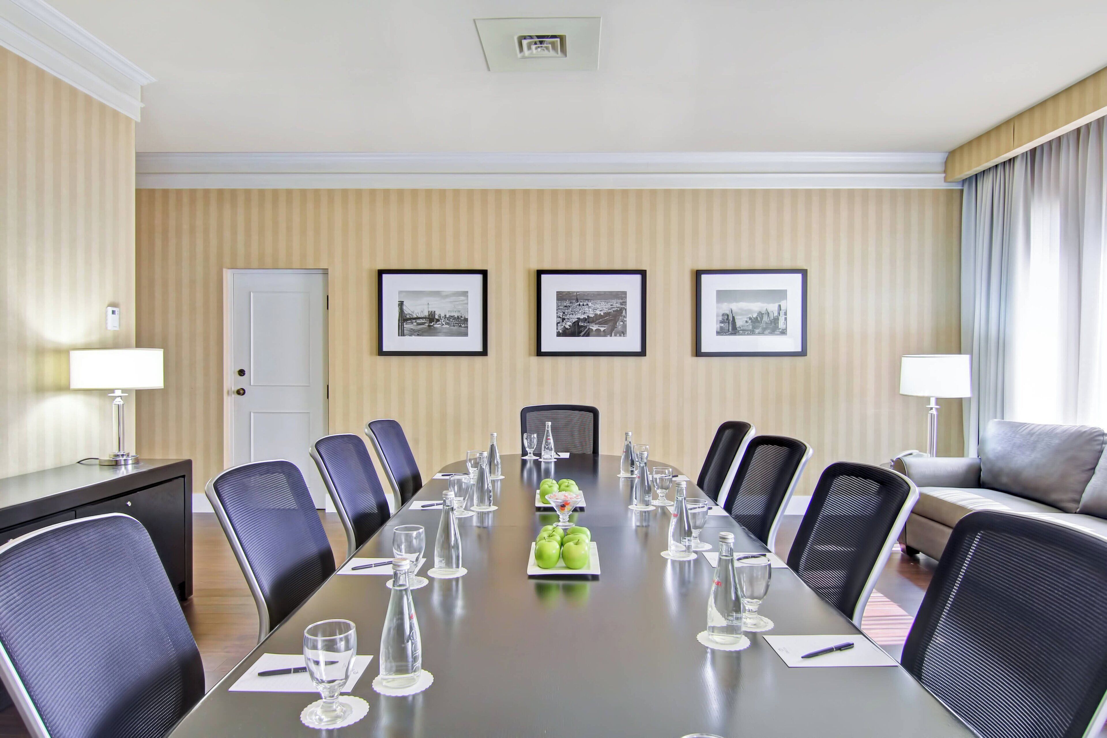 Una sala conferenze con un lungo tavolo, sedie, quadri appesi al muro e un divano sullo sfondo.