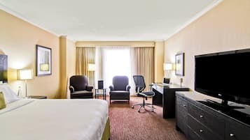 Ein Hotelzimmer mit einem großen Bett, zwei Sesseln, einem Schreibtisch mit Computer, einem Flachbildfernseher und einer Kommode.
