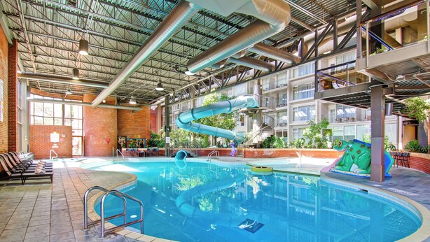 Une piscine intérieure avec un toboggan, une zone pour les plongeons en profondeur et un mur en briques.