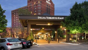 L’entrée d’un hôtel, avec un passage couvert, un espace de stationnement et un grand bâtiment portant l’enseigne « Delta Toronto East ».