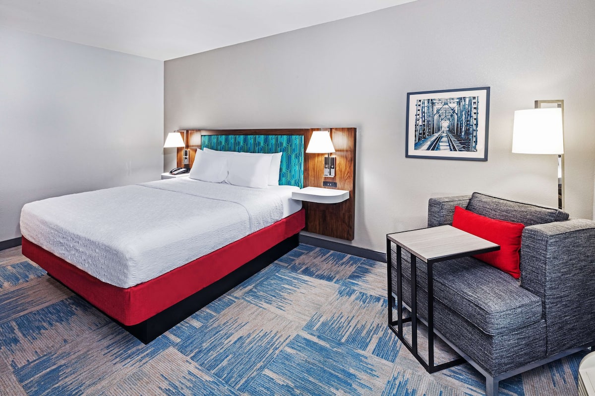 A hotel room with a bed, a sofa, a small table, two bedside lamps, and a framed picture on the wall.