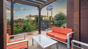 An outdoor patio area with a stone floor, orange cushioned seating, and a pergola structure. - Hampton Inn & Suites Houston Heights I-10 (Houston)