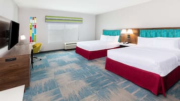 A hotel room with two beds, a desk, a TV, a lamp, and a window with blinds.