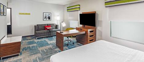 A modern hotel room with a bed, a desk, a chair, a sofa, a TV, and a window.