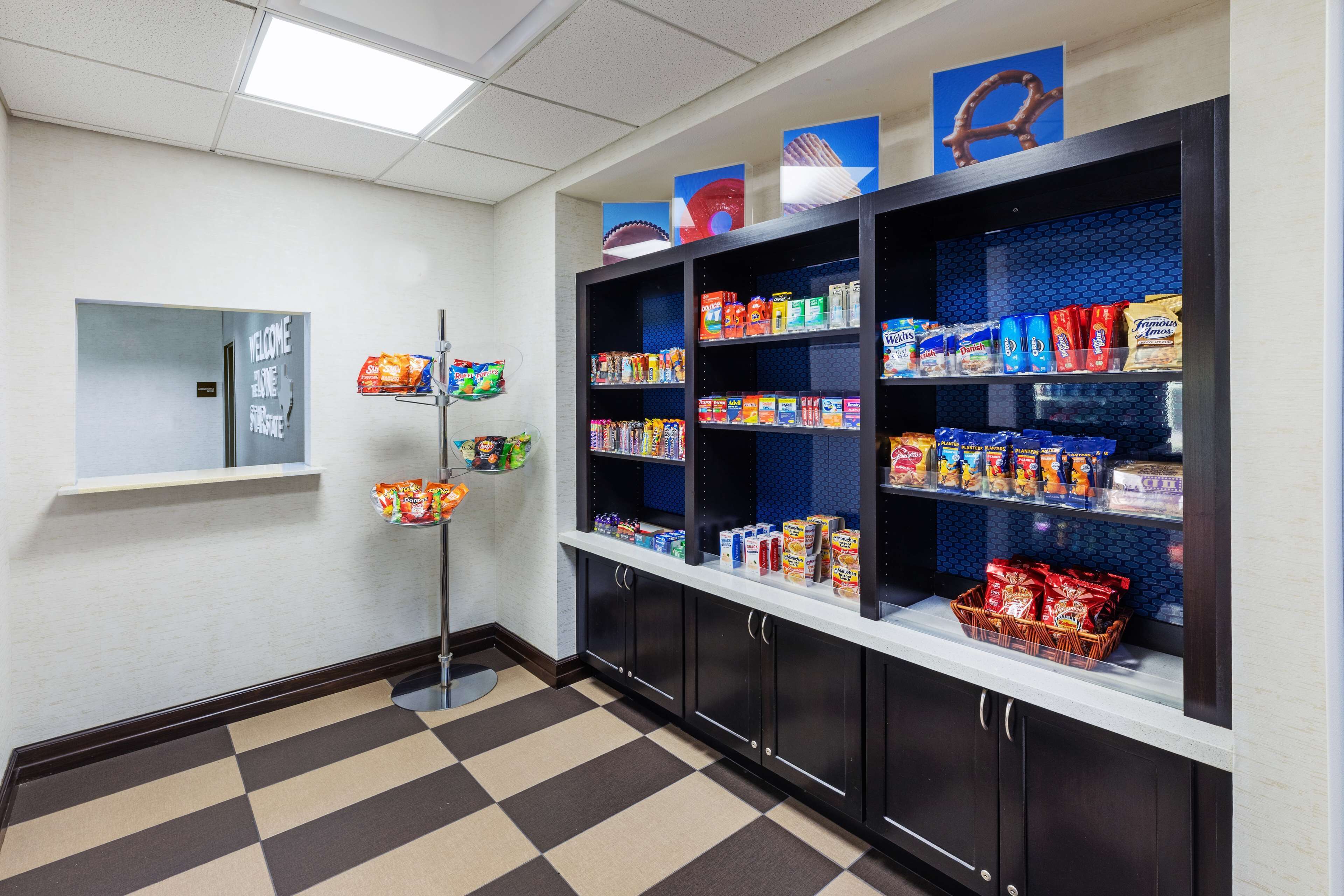 Un bar de aperitivos con estantes llenos de diversos snacks y bebidas envasadas, un letrero de bienvenida y un mostrador de recepción.