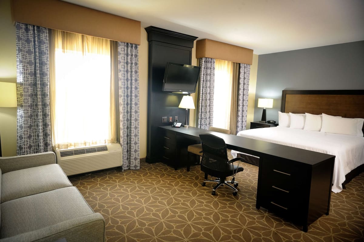 A hotel room with a bed, desk, chair, TV, and a window with curtains.