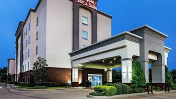 Edificio de Hampton Inn & Suites con entrada despejada, un cartel con el nombre y cielo claro.