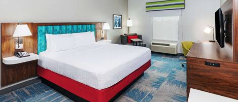 A hotel room with a large bed, a desk, a chair, a TV, and a window.