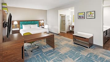 Une chambre d’hôtel avec un lit, un bureau, une chaise et une salle de bain visible à travers une porte ouverte.