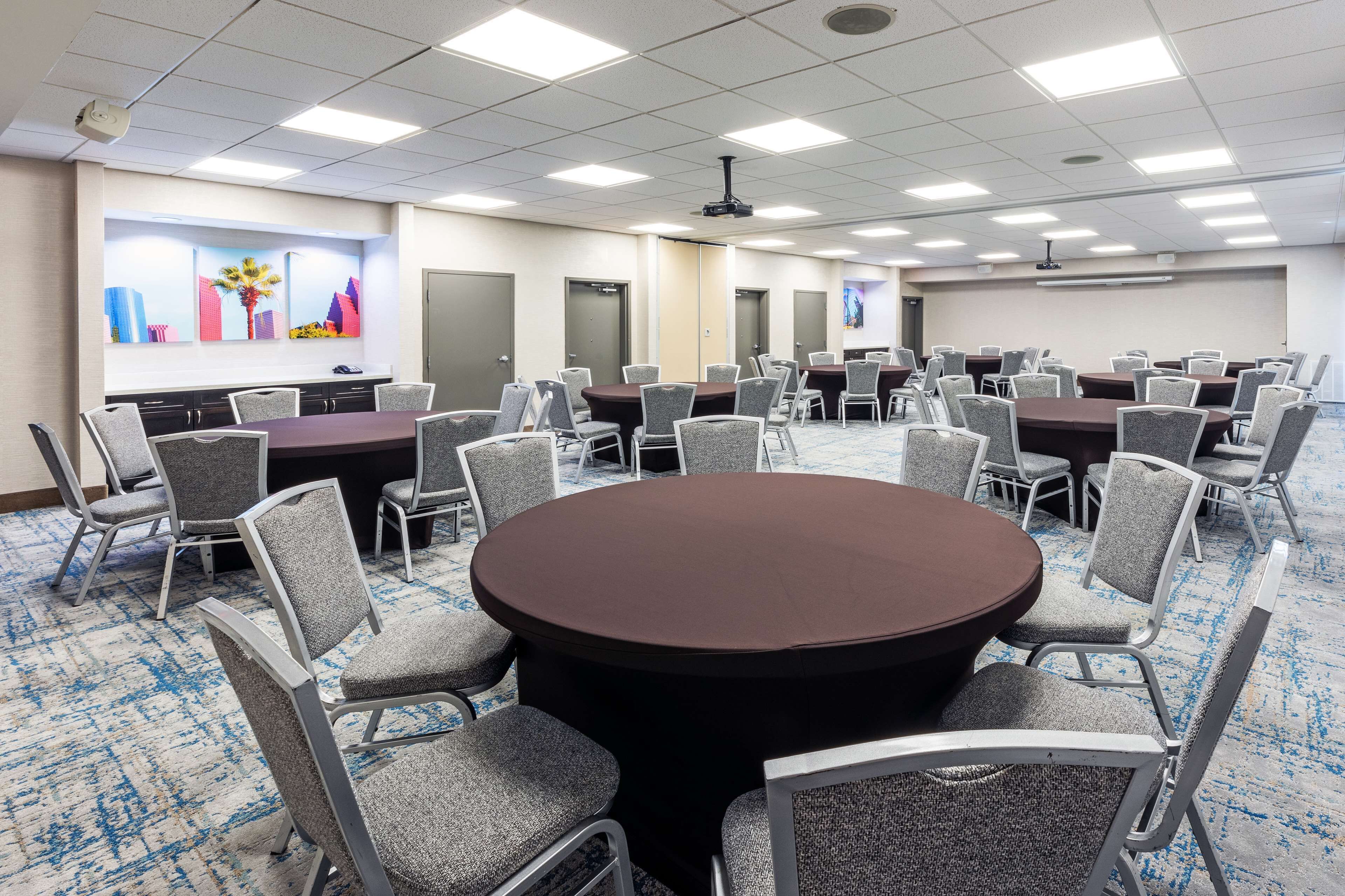A conference room with multiple tables and chairs, a projector screen, and a carpeted floor.